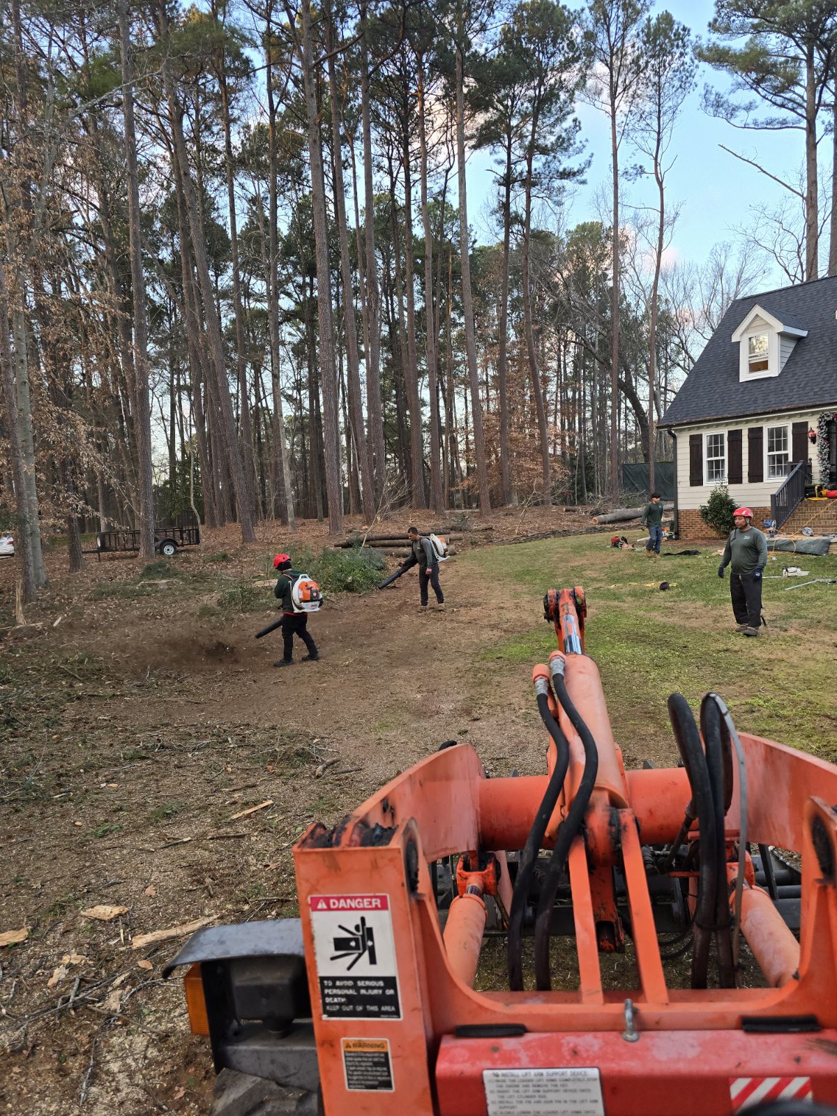 Yard debris removal crew raking and blowing beside a grapple loader in Wake County, NC